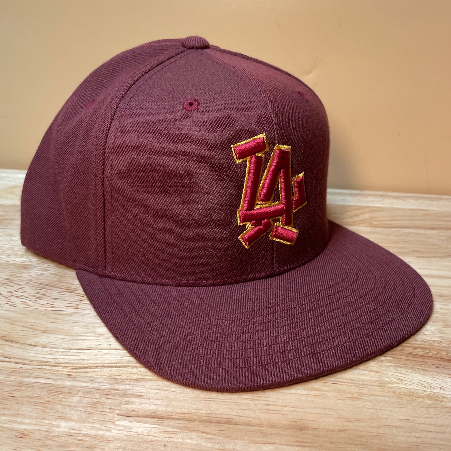 Maroon baseball cap with a logo on a wooden surface